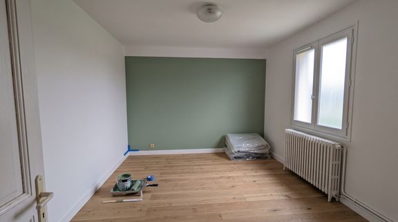 Chambre après travaux : murs blancs, un mur peint en vert sauge, parquet chêne clair posé et plinthes blanches