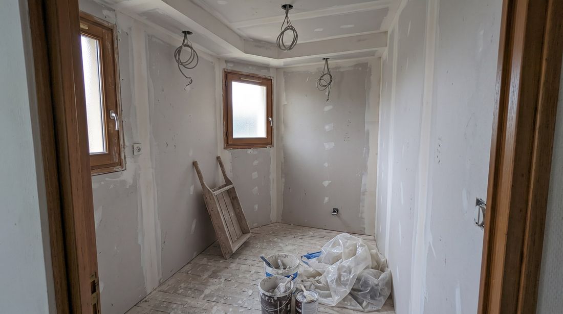Pièce en travaux : cloisons et plafond en plaques de plâtre, bandes et enduit en cours de finition, pots d'enduit posés au sol