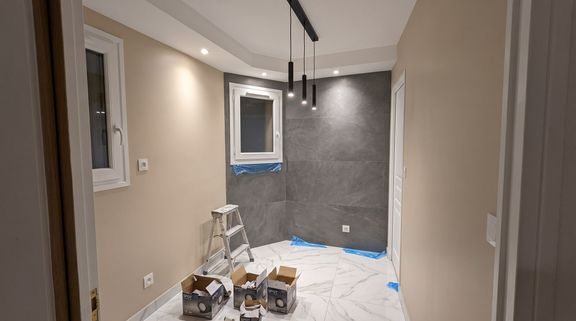Entrée en fin de chantier : sol en carrelage effet marbre blanc, pan de mur en carrelage gris grand format, plafond avec spots encastrés et suspensions noires