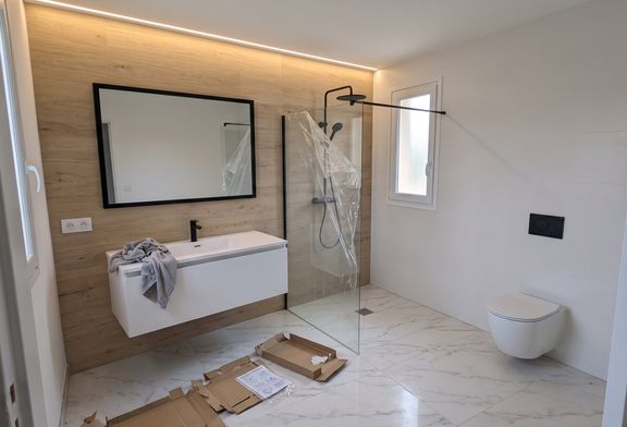 Salle de bain en fin de chantier : sol en carrelage effet marbre, mur en carrelage effet bois, douche à l'italienne avec caniveau et paroi vitrée, WC suspendu